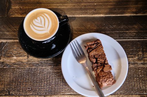 A high angle shot of a cup of coffee and plate of chocolate cake on a wooden table