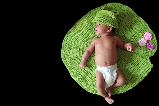 A top view of a baby with a green hat lying on a green blanket with a dark background