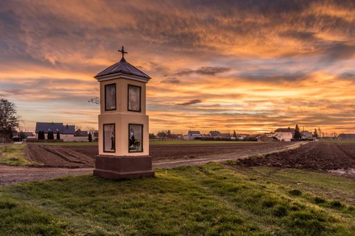 A small church with religious statues in a rural area at sunset