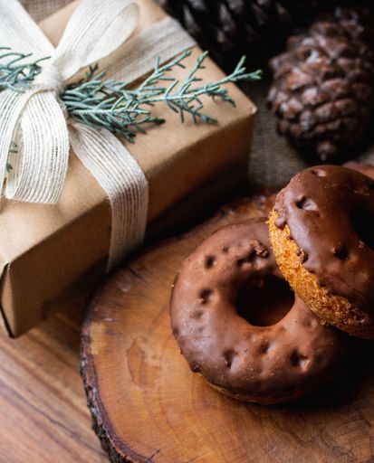 An overhead shot of chocolate-dipped doughnuts on a wooden board and wooden surface next to a wrapped gift