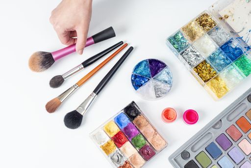 A high angle shot of brushes, acrylic powders, eyeshadow, and watercolor palettes with glitters