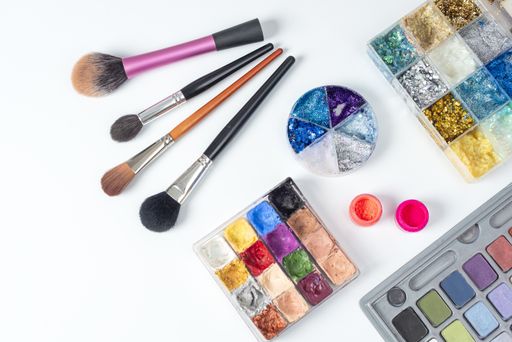 A high angle shot of brushes, acrylic powders, eyeshadow, and watercolor palettes with glitters