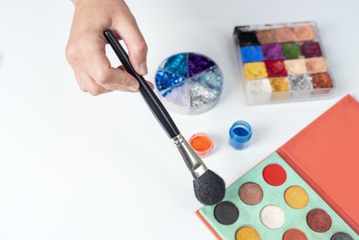 A selective focus shot of a hand holding a fluffy brush above an eyeshadow palette