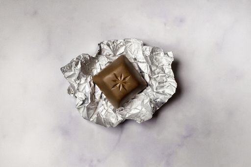 An overhead shot of a single chocolate block on a piece of foil on a marble surface