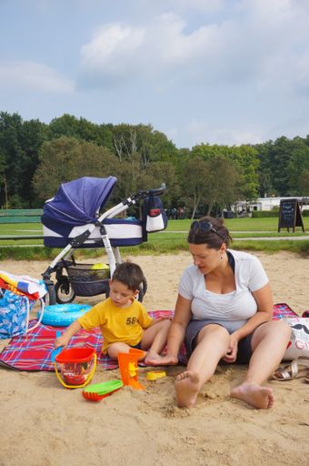 Woman and toddler boy sitting on a blanket and playing with toys at the Rosalka lake beach.