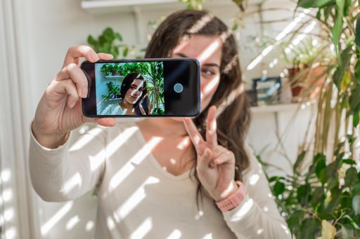A young girl posing on the balcony at home, taking a selfie and showing two fingers
