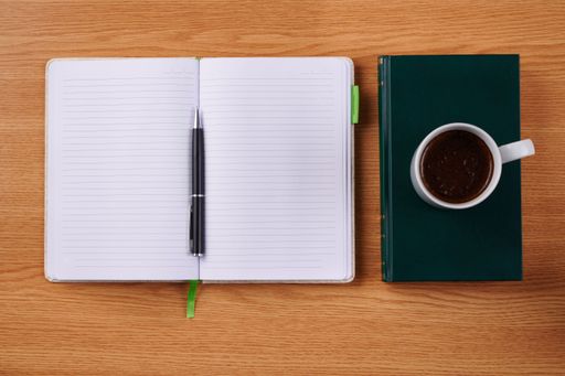Plain Blank Notebooks And A Pen Beside A Cup Of Coffee Placed Book Table. Simple Empty Notepads With A Ballpen And Mug Over Dictionary Desk.