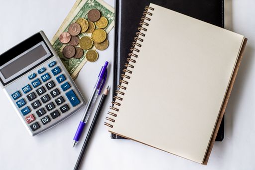 Plain Spiral Notebook With Pen Beside Calculator And Coins On Table. Simple Notepad And Ballpen Alongside Calculation Machine Placed On Top Of Desk.
