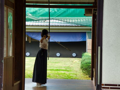 A girl holding bow and arrow and aiming at a target in a garden