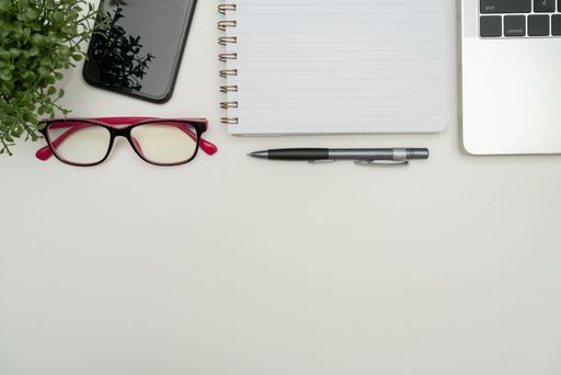 Office Supplies Over Desk With Keyboard And Glasses And Coffee Cup For Working Remotely, Assorted School Utilities With Hot Drink And Eyeglasses.
