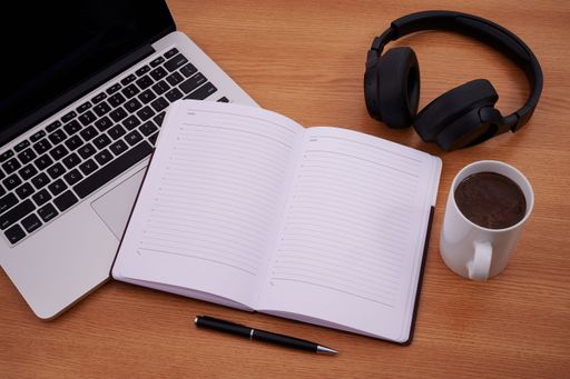 Blank Notepad Over Laptop With Cup Of Warm Coffee. Empty Journal On A Notebook Computer With A Ballpen And Headset Close To Mug Of Hot Drink.