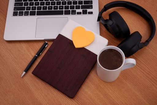 Blank Notepad Over Laptop With Cup Of Warm Coffee. Empty Journal On A Notebook Computer With A Ballpen And Headset Close To Mug Of Hot Drink.