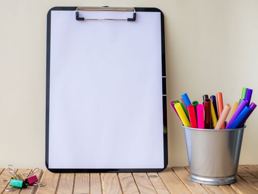 Plain Office Clipboard With Stack Of Pens In A Holder On Top Of A Table. Empty Paper Sheet With Colorful Pencils Container Placed On A Desk.