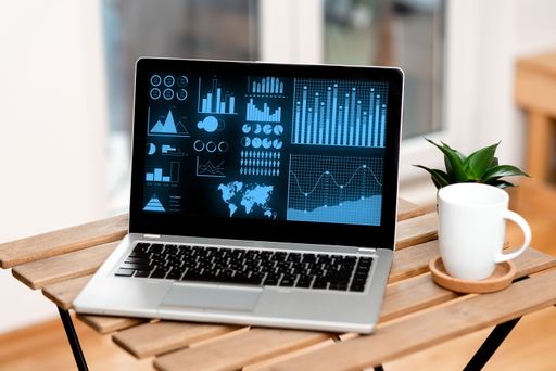 Laptop On A Table Beside Coffee Mug And Plant Showing Work Process. Sitted Top Of Desk Next To Cup Along With Flower Displaying Remote Job Projects.