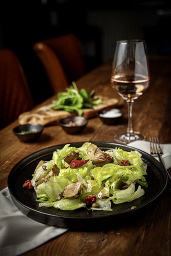 A vertical shot of a salad served on a black plate with a glass of wine