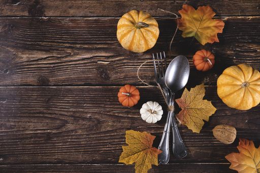 A top view of fresh pumpkins, walnuts, autumn leaves with a fork and spoon on a wooden background