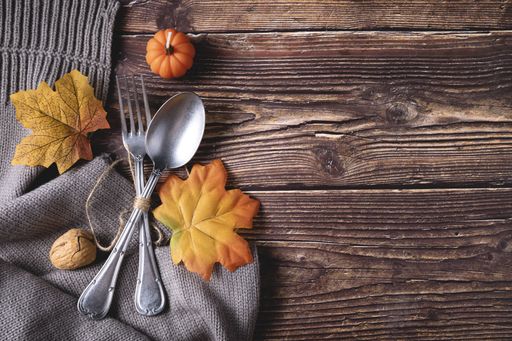 A top view of fresh pumpkin, walnut, autumn leaves with fork and spoon on a gray blanket