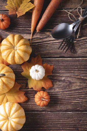 A top view of fresh pumpkins, carrots, and autumn leaves on a wooden background
