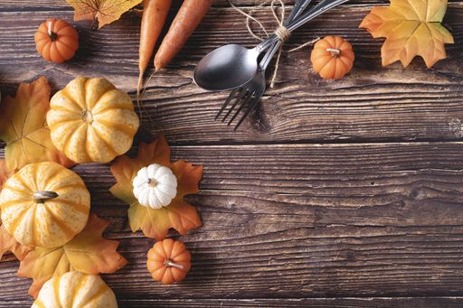 A top view of fresh pumpkins, carrots, and autumn leaves on a wooden background