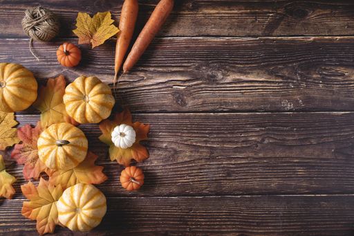 A top view of fresh pumpkins, carrots, and autumn leaves on a wooden background