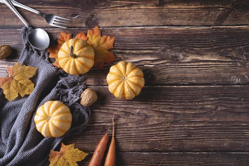 A top view of fresh pumpkins, walnuts, and autumn leaves on a gray blanket