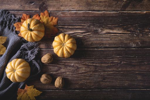 A top view of fresh pumpkins, walnuts, and autumn leaves on a gray blanket