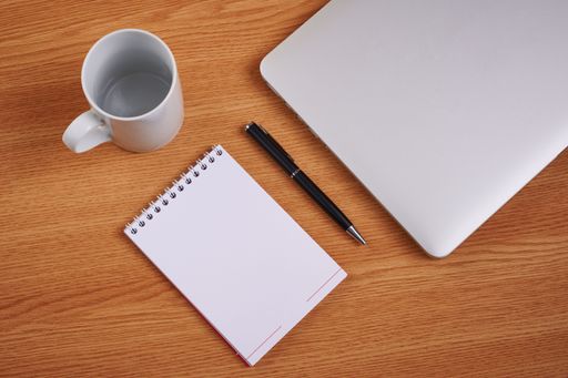 Closed Laptop Beside Empty Journal With Pen And Coffee Mug Over Table. Notebook Computer With Blank Notepad Ballpen Beside Cup Placed Above Work Desk.