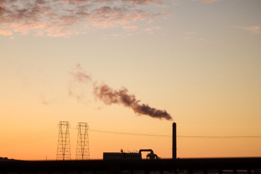 A wide shot of a factory with smoke coming out of a tall pipe - global warming