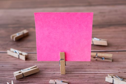 Blank Square Note Surrounded By Laundry Clips Showing New Meaning. Empty Piece Of Sticky Paper Clipped Upright Placed On Top Of Wooden Table