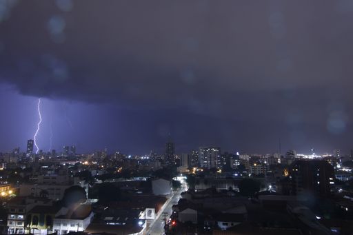 A thunderstorm with lightning in a cloudy sky at night over the urban area