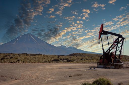 A closeup of an oil pump at large oilfields over the mountain range.