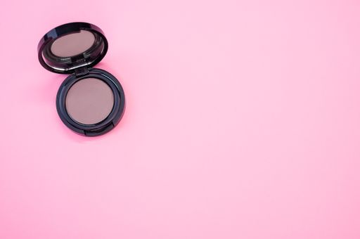 A top view of a pink single eyeshadow palette on a pink surface