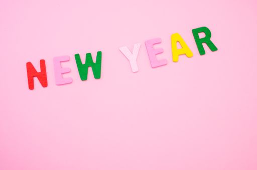 A top view of New Year written with colorful wooden letters on a pink surface