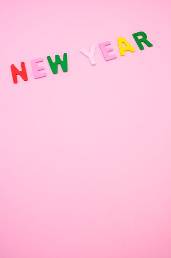A vertical shot of New Year written with colorful wooden letters on a pink surface
