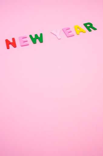 A vertical shot of New Year written with colorful wooden letters on a pink surface
