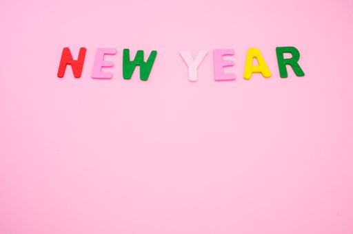 A top view of New Year written with colorful wooden letters on a pink surface