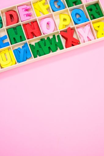 A vertical shot of colorful wooden letters in their case, placed on a pink surface