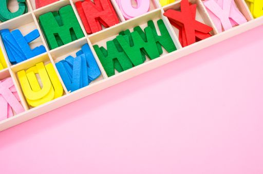A top view of colorful wooden letters in their case, placed on a pink surface