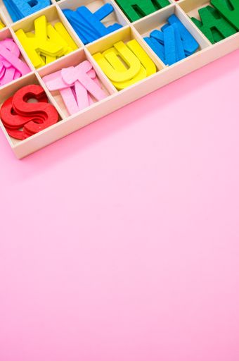 A vertical shot of colorful wooden letters in their case, placed on a pink surface