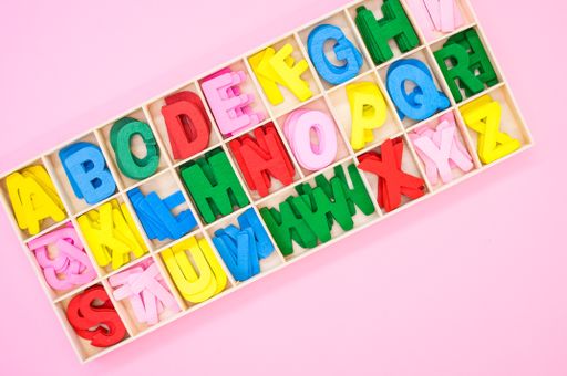 A top view of colorful wooden letters in their case, placed on a pink surface