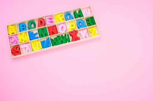 A top view of colorful wooden letters in their case, placed on a pink surface