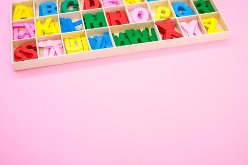 A high angle of colorful wooden letters in their case, placed on a pink surface