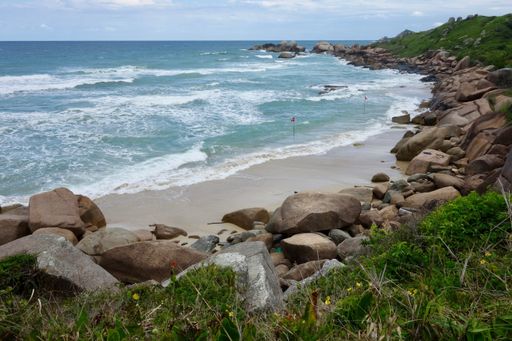 A landscape of a sea surrounded by greenery and rocks under sunlight in Brazil