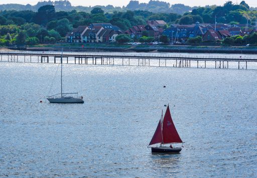 Two sailboats are sailing past a bridge in Portsmouth Harbour, United Kingdom.