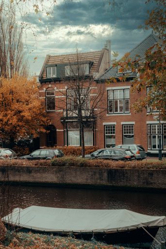 A vertical shot of a channel surrounded by cars and buildings under a cloudy sky in the Netherlands