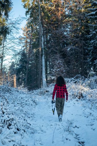 A vertical shot of a female walking through the forest covered with snow