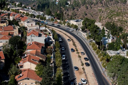 A road surrounded by buildings and hills covered in greenery under the sunlight during daytime