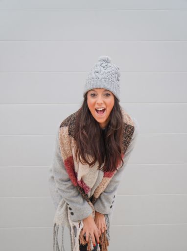 A happy young caucasian female wearing a winter coat and a hat posing against a white wall