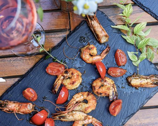 A top view of fried shrimps served on black Charcuterie board with wine on a wooden table