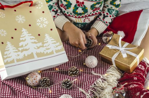 A view of a woman in a Christmas sweater holding a pine cone in her hands sitting on the bed